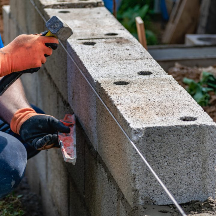 A bricklayer works on blocks to build a wall on a construction site with concrete, a trowel, a level and a grinder